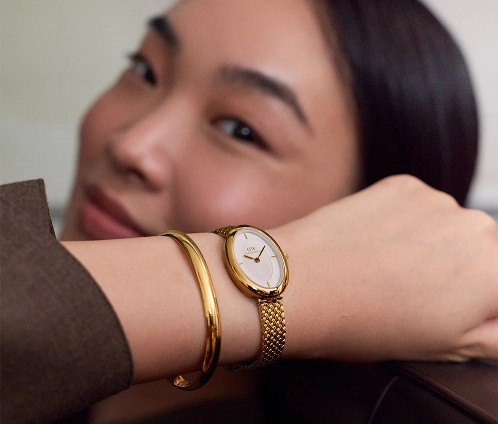 Smiling model resting an arm with a gold bangle and a white dial watch